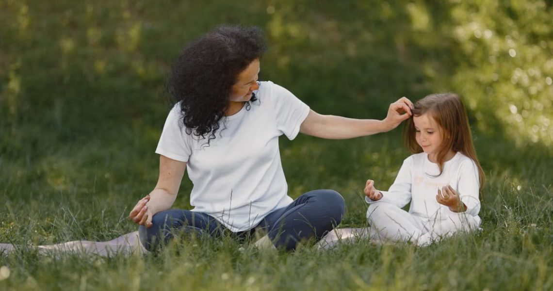 Mother and daughter bonding through yoga outdoors in a serene grassy field.